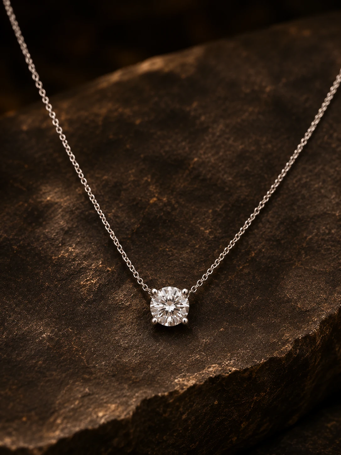 Round diamond pendant on a fine silver-tone chain resting on dark stone
